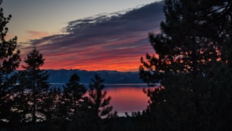 Sunset view over a serene mountain lake with reflections of pine trees.