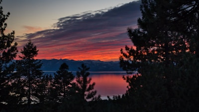 A vibrant sunset over a quiet mountain lake, reflecting fiery orange and pink hues.
