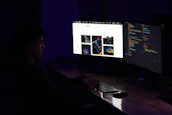 A close-up of a person engaged in cyber training, illuminated by multiple monitors displaying security data.