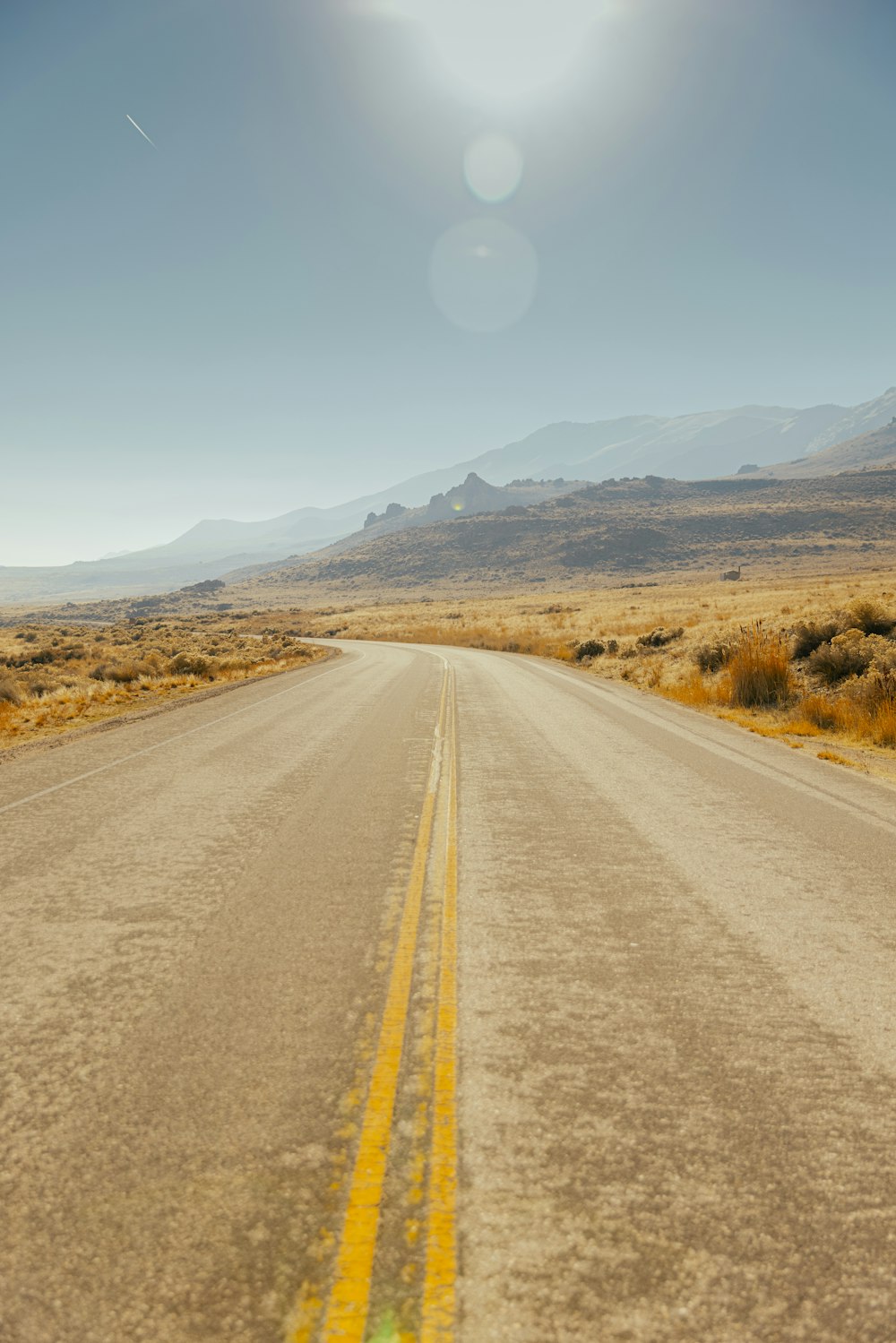 gray asphalt road between brown grass field during daytime