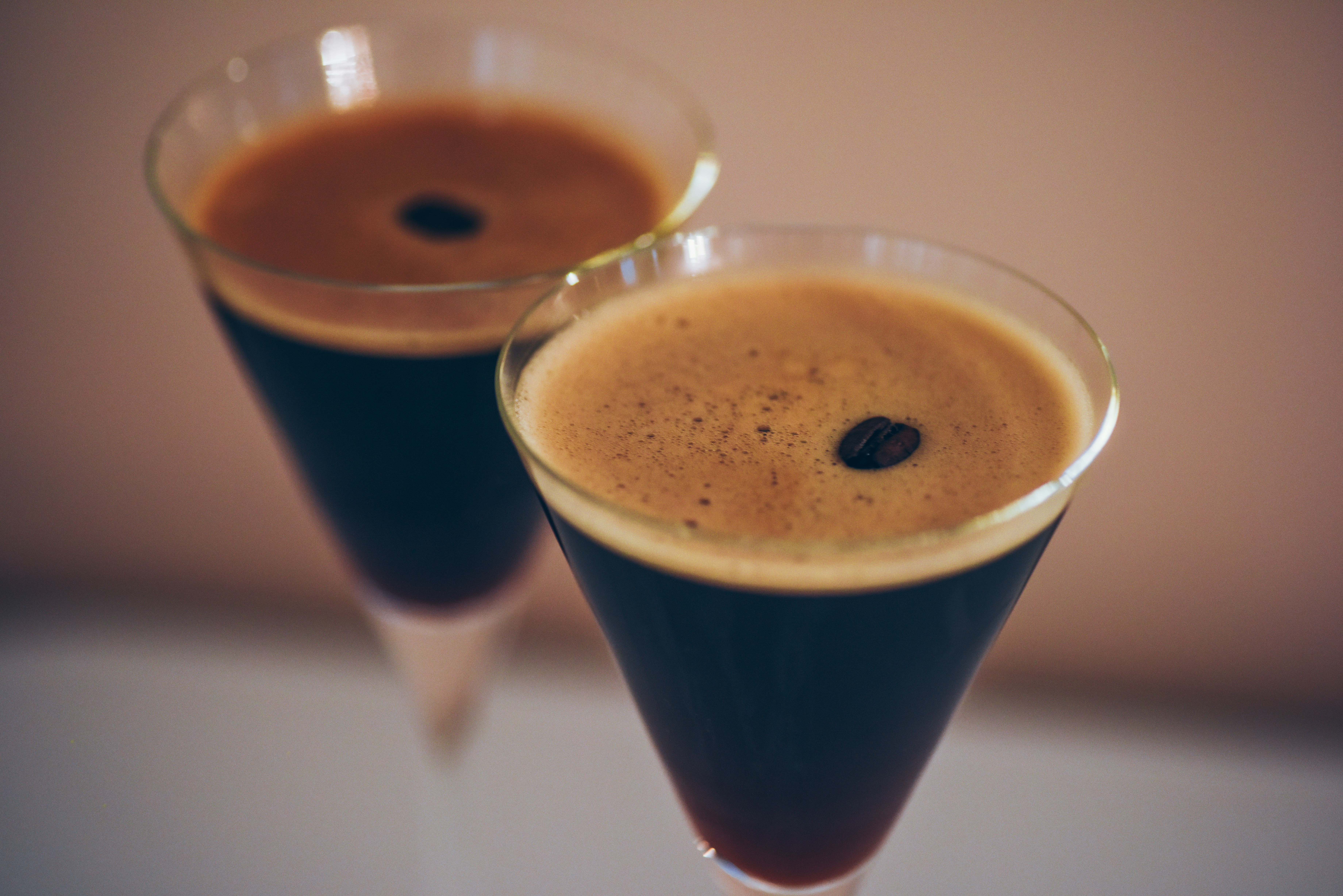 Non-alcoholic espresso martini with creamy foam and coffee bean garnish in two martini glasses on neutral background