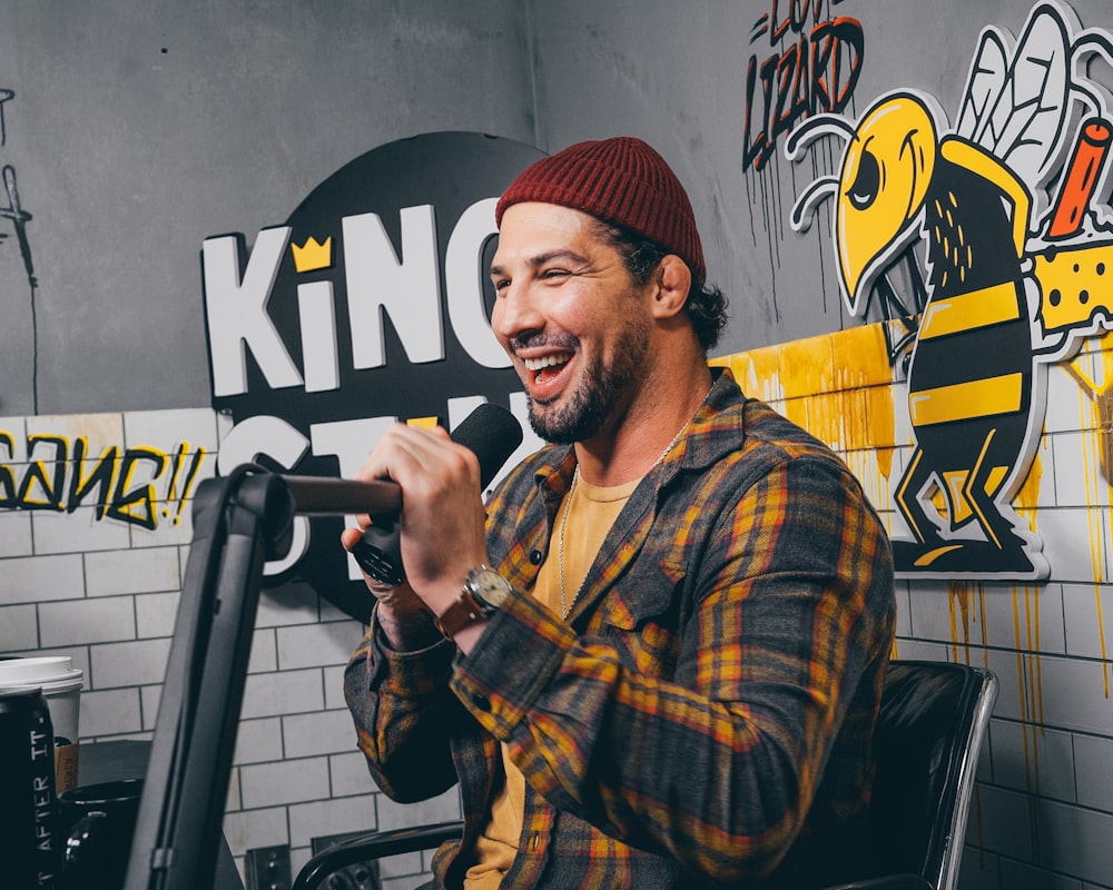 man in red knit cap and yellow and black plaid dress shirt holding microphone