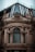 A richly adorned architectural facade features intricate sculptures and ornate carvings surrounding a large, arched window. The top section includes modern glass panels and metal framing, creating a contrast between classical and contemporary design elements.