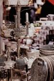 A display of intricately patterned ceramic bowls, teapots, and dishes organized on metallic shelves, all with a monochromatic color scheme featuring polka dots and stripes. Glass candlesticks and decorative items also appear on the shelves in an indoor store setting.