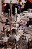 A display of intricately patterned ceramic bowls, teapots, and dishes organized on metallic shelves, all with a monochromatic color scheme featuring polka dots and stripes. Glass candlesticks and decorative items also appear on the shelves in an indoor store setting.