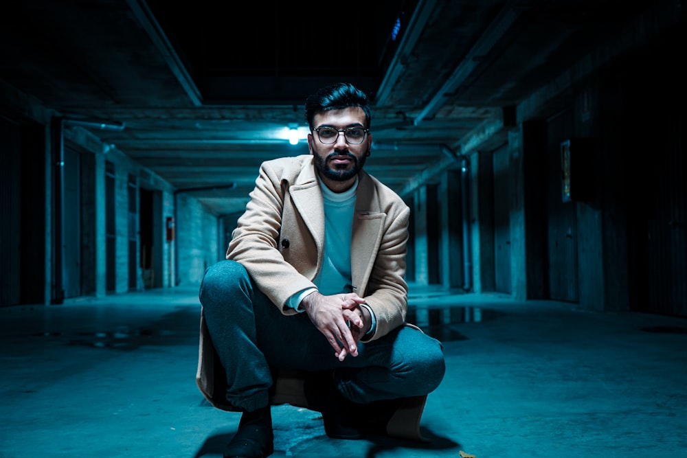 man in brown suit jacket and blue denim jeans sitting on blue floor