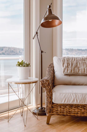 A sunlit living room corner featuring a sleek metal side table beside a plush cotton bath mat and a soft linen shower curtain.