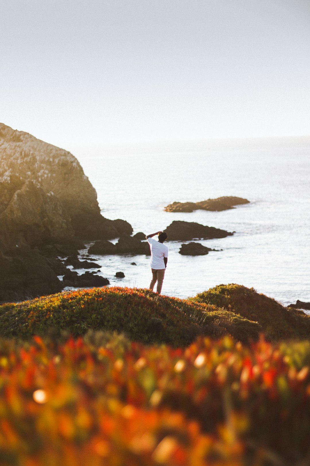 2 people standing on the rock near the ocean during daytime