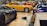 A collection of luxury sports cars are displayed in an indoor showroom with a polished wooden floor. The focus is on a vintage yellow car surrounded by modern vehicles of various colors, including red, blue, and gray. The setting appears affluent and neatly organized, highlighting the elegance and design of each car.