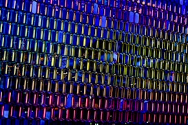 A vibrant and colorful pattern of hexagonal glass panels with reflections of light creating a dynamic, kaleidoscope effect. The panels display a spectrum of colors from deep blues and purples to bright yellows and reds, generating an abstract and mesmerizing design.