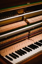 The image displays the interior mechanism of an upright piano, focusing on the hammers, strings, and the keyboard. The wooden hammers are aligned in rows, and the black and white keys of the keyboard are visible at the bottom.