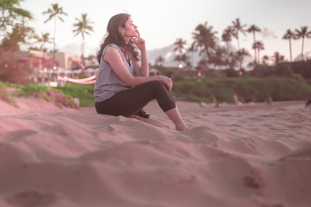 woman in pink tank top and black pants sitting on pink sand during daytime