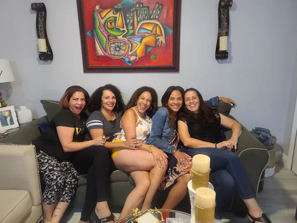 A group of diverse young women sharing a joyful moment in a cozy community room filled with colorful artwork.