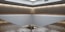 A minimalist interior space with a high ceiling and light gray walls. A horizontal wooden beam divides the upper and lower sections. Recessed lighting around the ceiling creates a soft, warm glow. The architecture features clean lines and a modern design with an open and spacious feel.