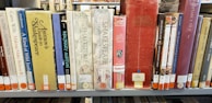 A row of books on a library shelf, featuring various titles related to Shakespeare and other literary topics. The books are in a mix of colors, and there are labels on the spines indicating their library classification.