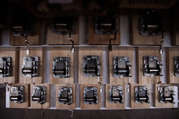A collection of mechanical music boxes with metal and wooden components arranged in rows. The devices have cranks for operation and are mounted on wooden bases, giving a vintage and intricate appearance.