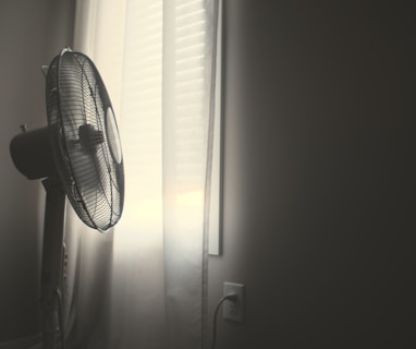 white wall fan turned on near white window blinds