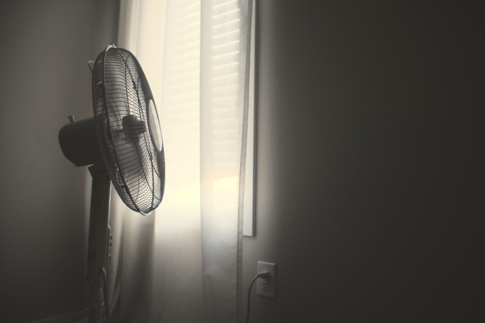 Ventilador de pared blanco encendido cerca de persianas blancas