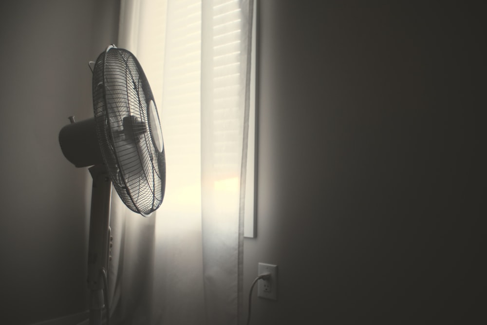 white wall fan turned on near white window blinds