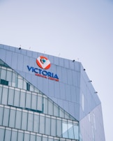 Modern multi-story building with a prominent sign for Victoria Medical Center on its upper facade. The building features sleek glass and metal architecture with evenly spaced windows, and the sky in the background is clear and blue.