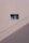 A simple beige wall with a small rectangular window, featuring a sliding design. The wall's texture appears rough and paint has subtle cracks. A shadow, likely from a utility line or similar object, diagonally crosses the bottom section of the image.