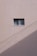 A simple beige wall with a small rectangular window, featuring a sliding design. The wall's texture appears rough and paint has subtle cracks. A shadow, likely from a utility line or similar object, diagonally crosses the bottom section of the image.