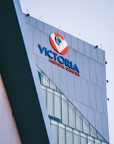 A modern building facade with large glass windows, prominently displaying signage for a medical center in bold blue and red colors against a sleek grey exterior.