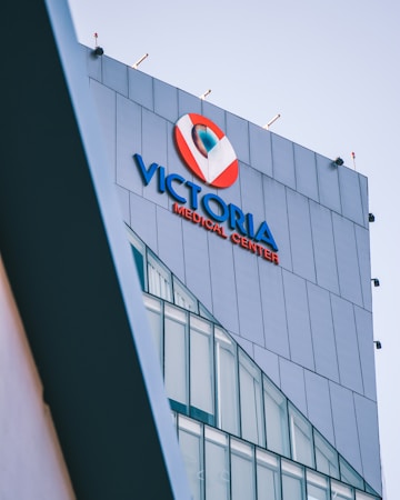 A modern building facade with large glass windows, prominently displaying signage for a medical center in bold blue and red colors against a sleek grey exterior.