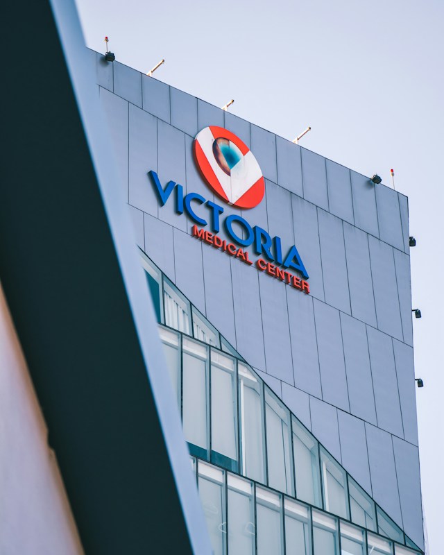 A modern building facade with large glass windows, prominently displaying signage for a medical center in bold blue and red colors against a sleek grey exterior.