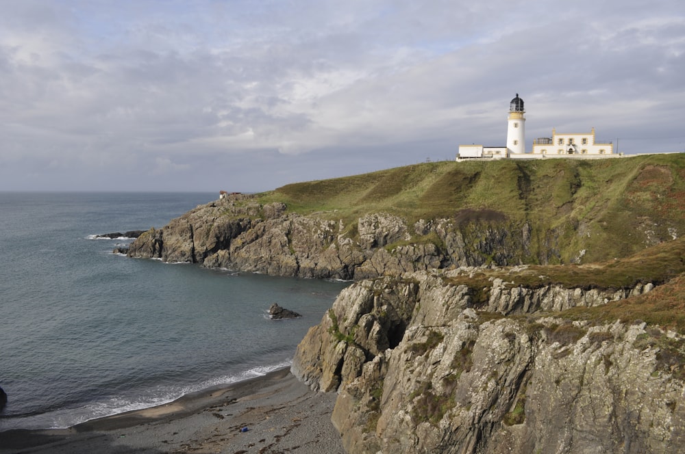 white lighthouse on brown rocky mountain beside body of water during daytime