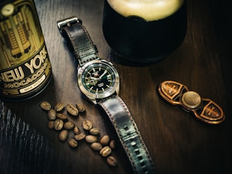 silver round analog watch with black leather strap beside brown coffee beans