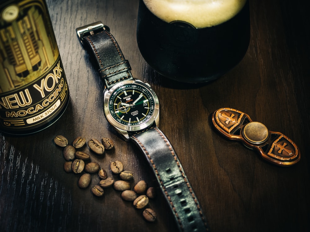 silver round analog watch with black leather strap beside brown coffee beans