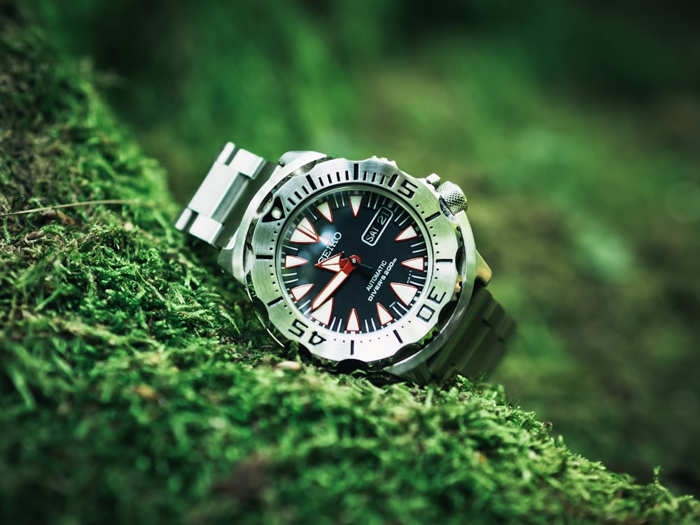 round silver analog watch with white strap on green grass
