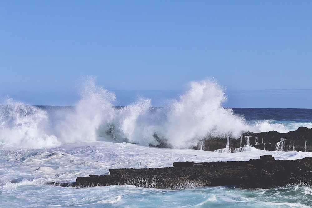 ocean waves crashing on rock formation under blue sky during daytime