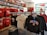 A retail display in a store features Stanford University merchandise, including red and grey t-shirts, hoodies, and sports equipment like basketballs and footballs on shelves and racks.