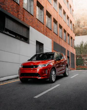 red car parked beside white concrete building during daytime