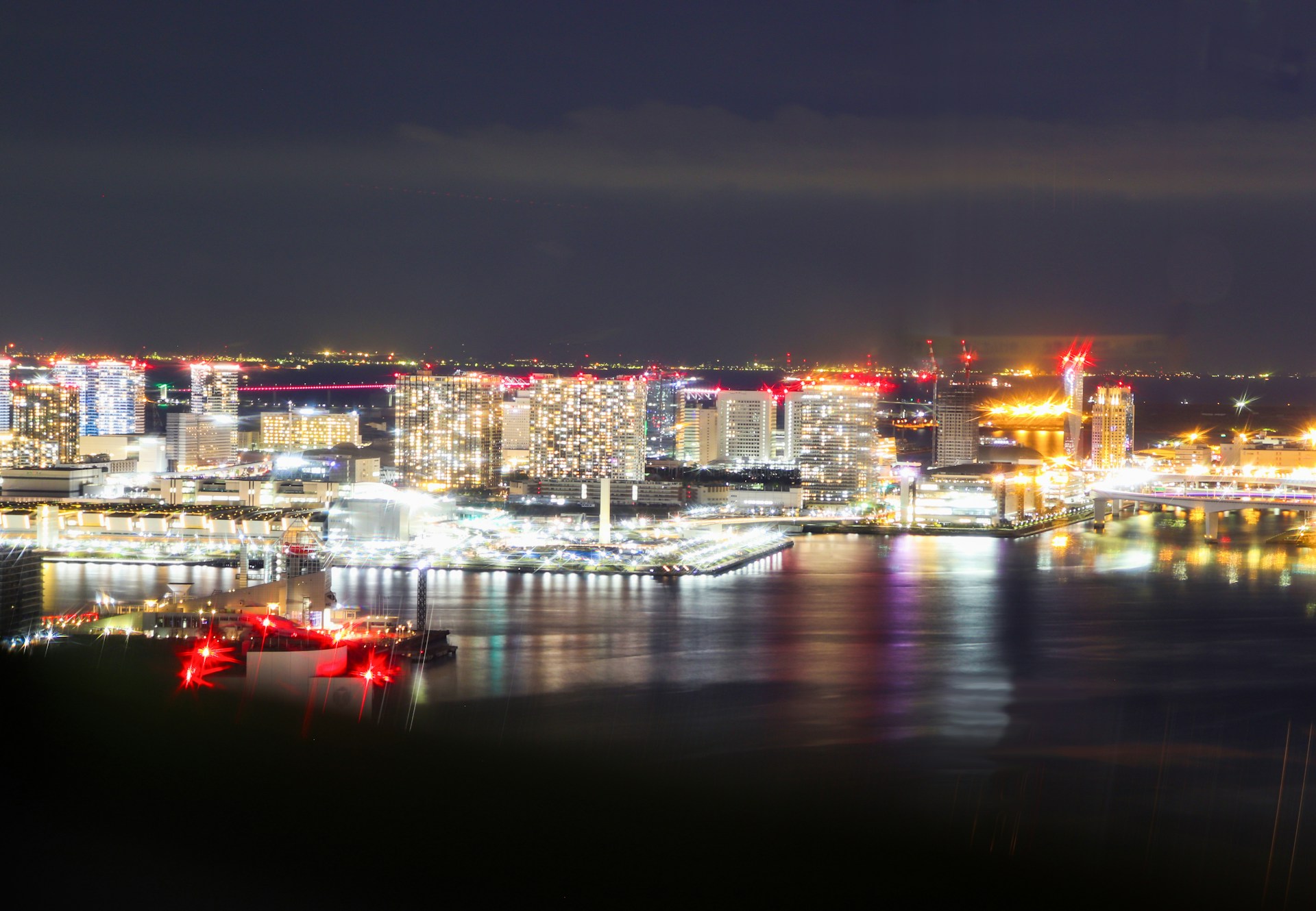 An elegant cityscape at night, with reflections on glass surfaces and a dark charcoal background highlighting the glowing white and red lights.
