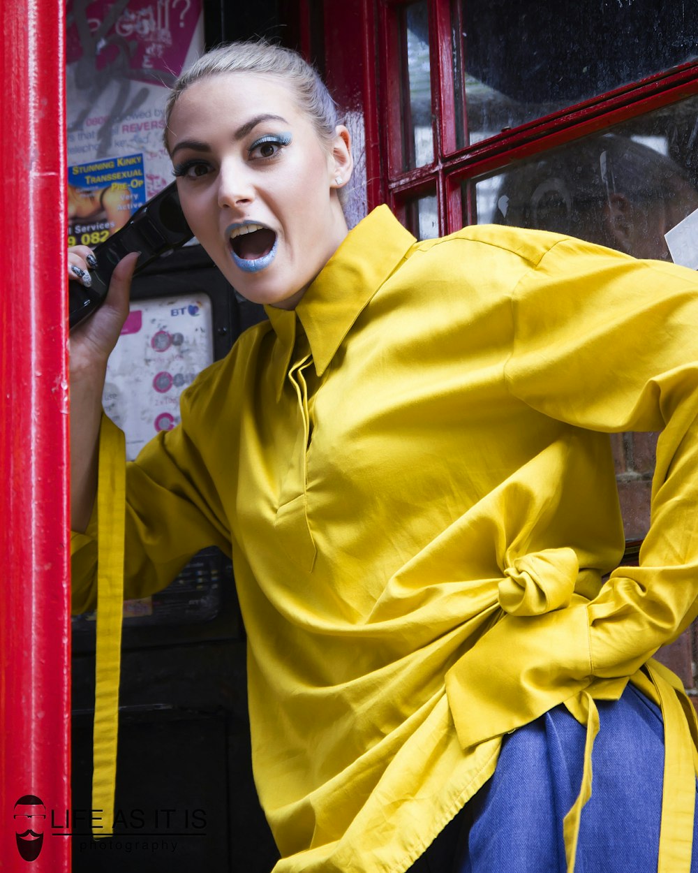 woman in yellow button up shirt standing beside red telephone booth