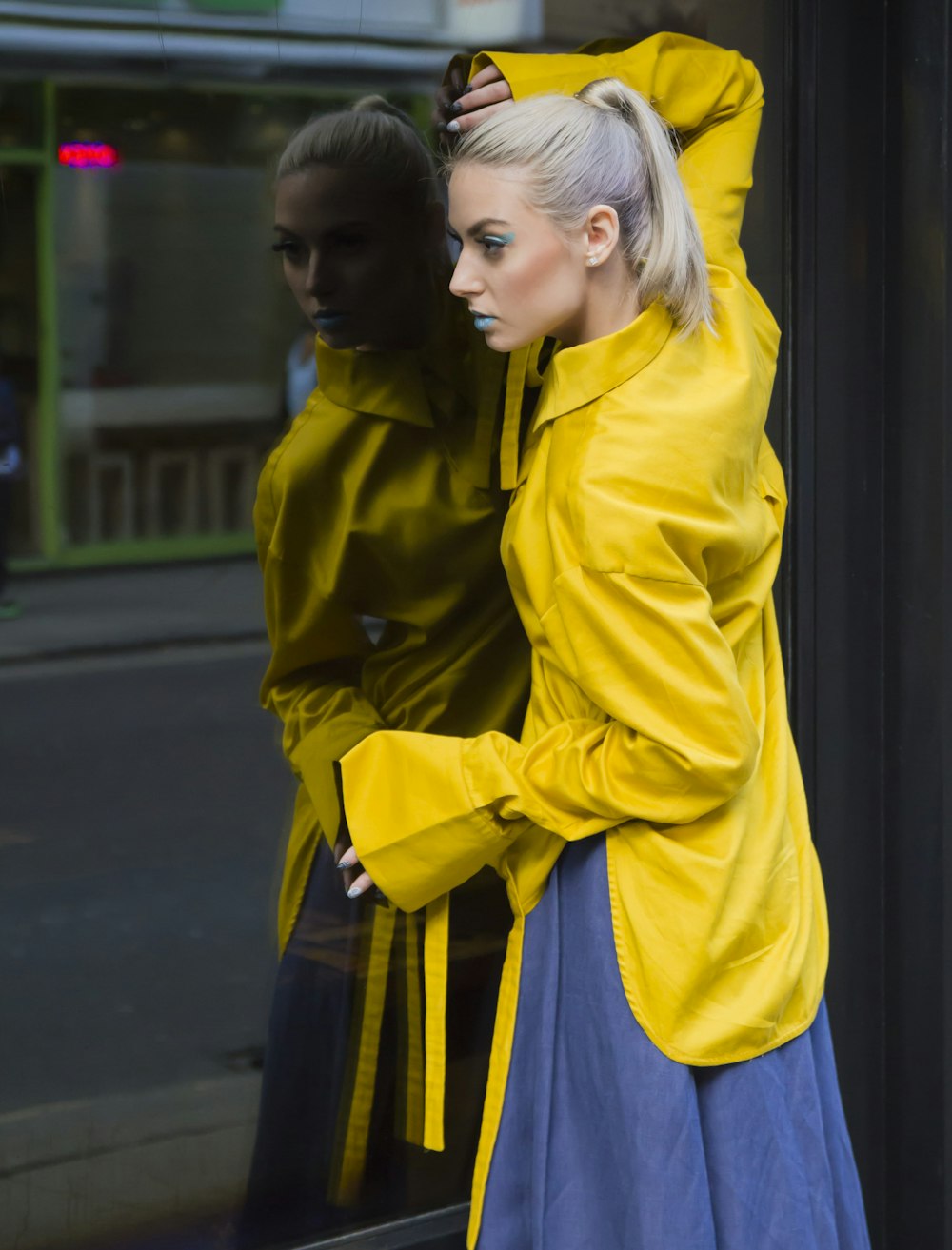 fille en veste jaune et jupe bleue debout sur le trottoir pendant la journée