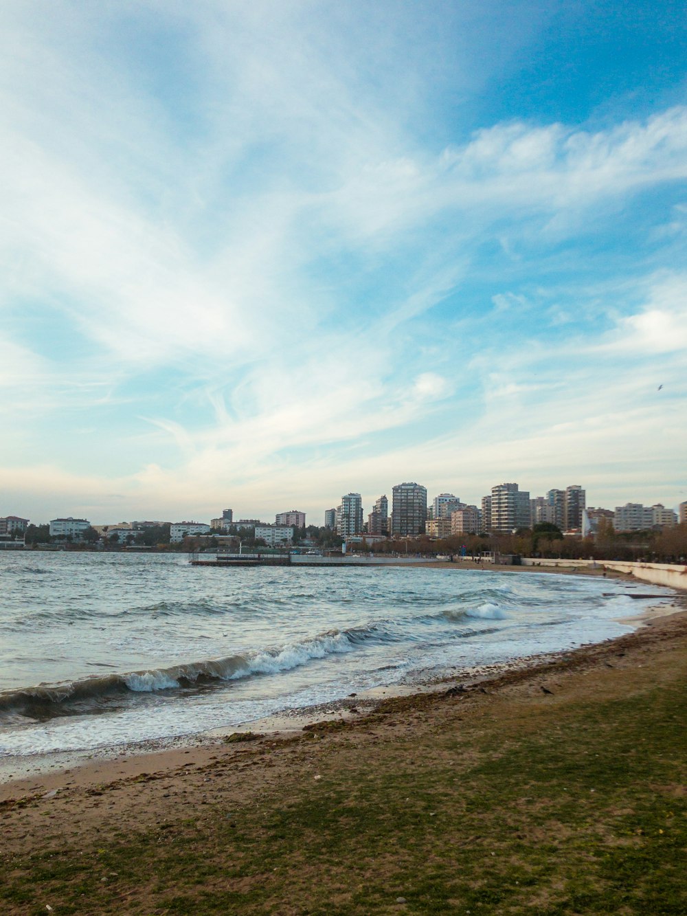 city skyline across sea under blue and white sunny cloudy sky during daytime