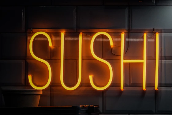 A sleek neon-lit sushi platter glowing in hot pink and cyan on a black background.