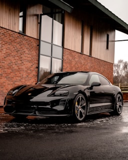 A sleek black and red sports car parked in front of a modern steel building under a clear sky.