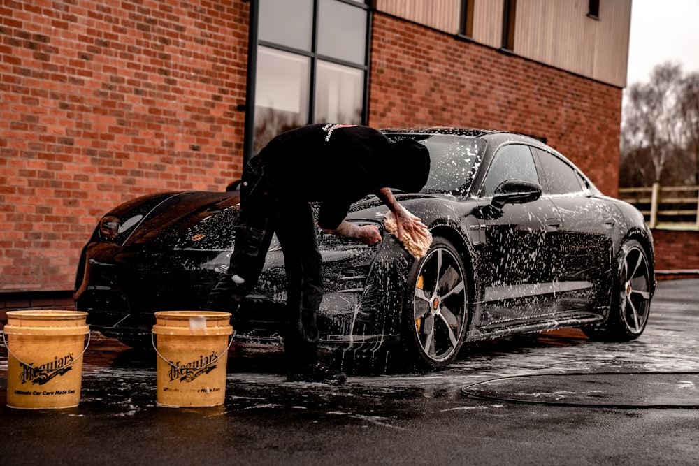 黒い車にもたれかかっている黒いジャケットとズボンの男