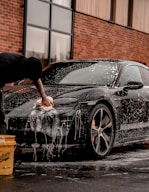 man in black t-shirt and black pants doing water splash on black coupe during daytime