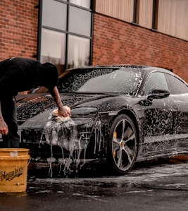 man in black t-shirt and black pants doing water splash on black coupe during daytime