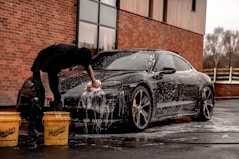 man in black t-shirt and black pants doing water splash on black coupe during daytime