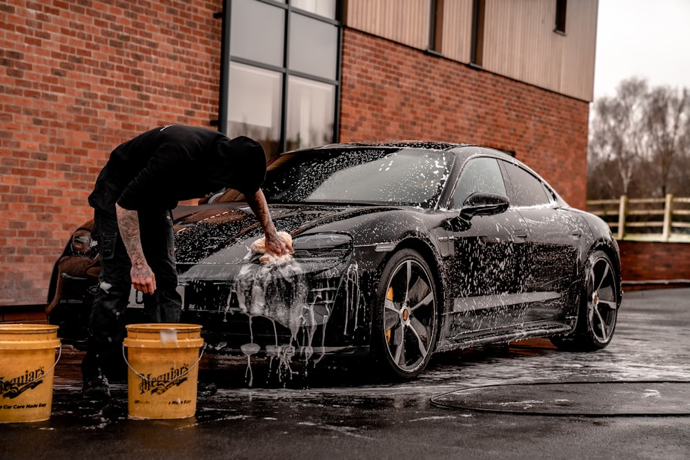 Mann in schwarzem T-Shirt und schwarzer Hose spritzt tagsüber Wasser auf schwarzem Coupé