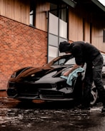 man in black jacket and blue denim jeans standing beside black bmw coupe