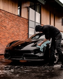 man in black jacket and blue denim jeans standing beside black bmw coupe