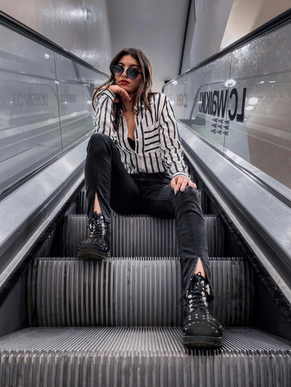 woman in black and white striped long sleeve shirt and black pants sitting on escalator